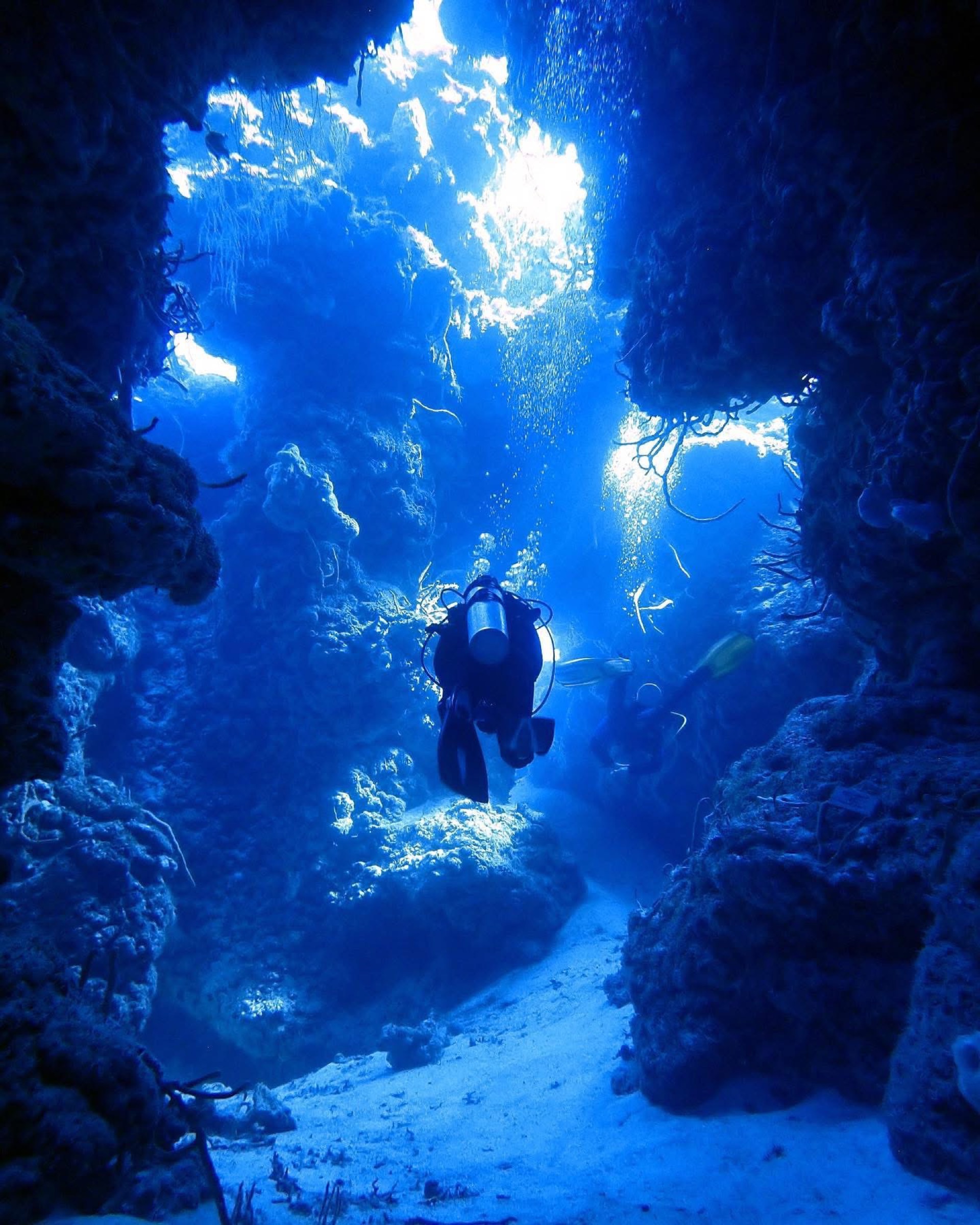 Scuba diver exploring an underwater cavern with light streaming in